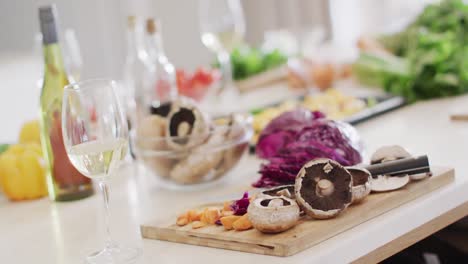 glasses of white wine and fresh vegetables on chopping board on kitchen counter top, slow motion