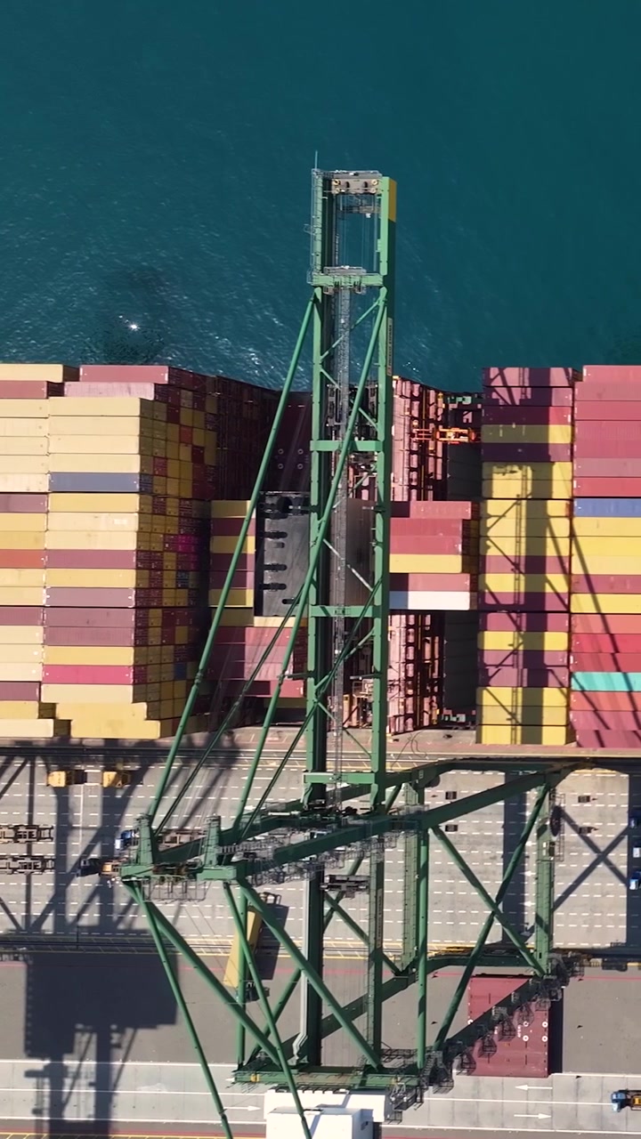 A container terminal with a large number of shipping containers stacked on the dock. Cranes are actively moving cargo in a busy global shipping hub.