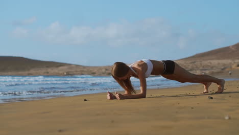 Vista-Lateral-De-Una-Hermosa-Mujer-Deportiva-En-Posición-De-Tabla-En-La-Playa-Durante-El-Atardecer.