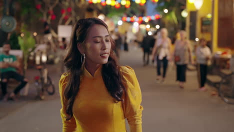 woman in vibrant yellow ao dai strolling through hoi an's lively evening market, lanterns glowing