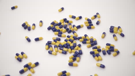 cámara lenta de pastillas azules y amarillas caídas sobre fondo blanco