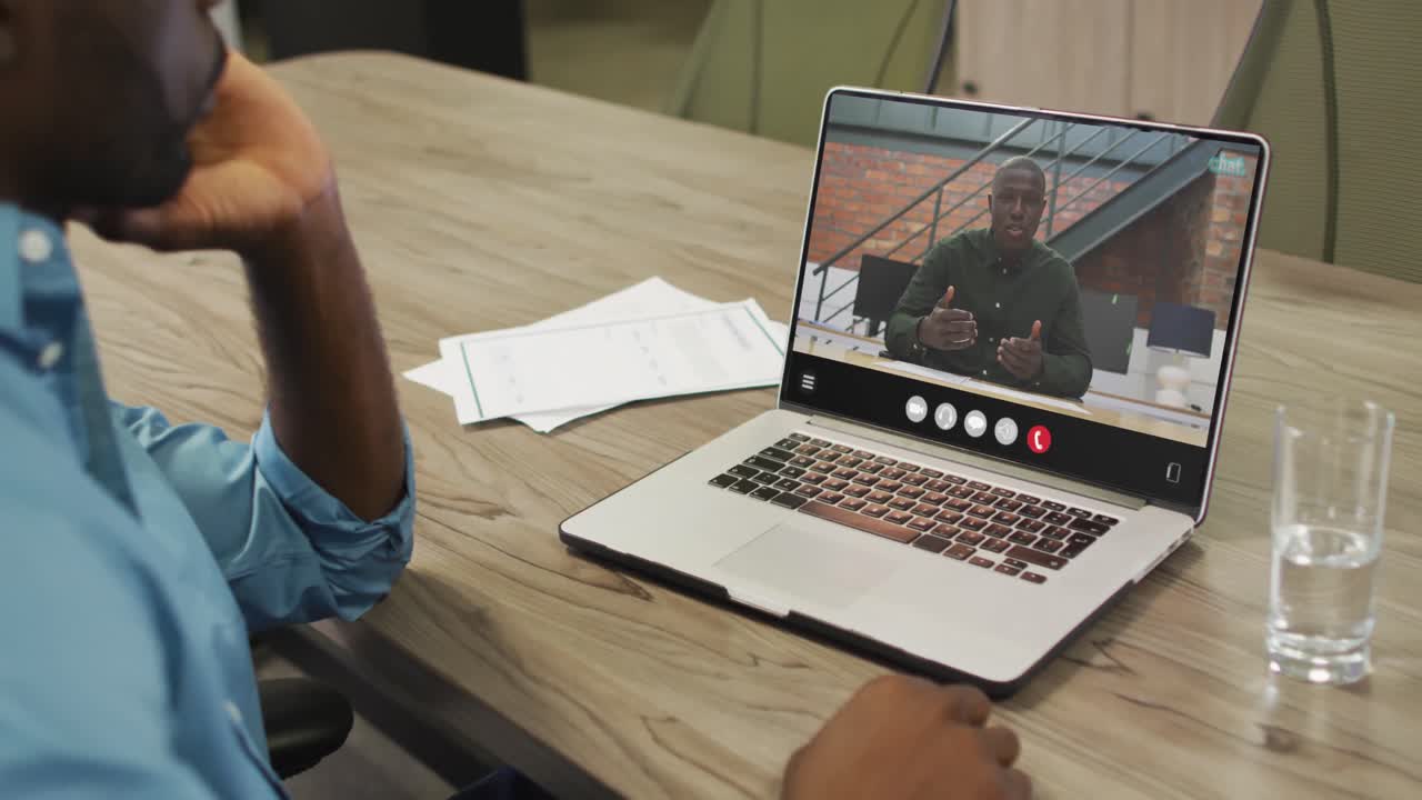hombre afroamericano usando una computadora portátil para una llamada de video, con un colega de negocios en la pantalla