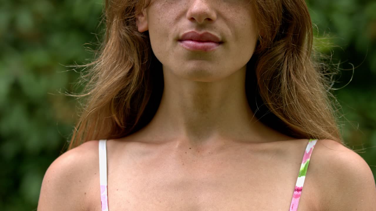 un primer plano de la parte superior del torso y la mitad inferior de la cara de una mujer contra un fondo verde