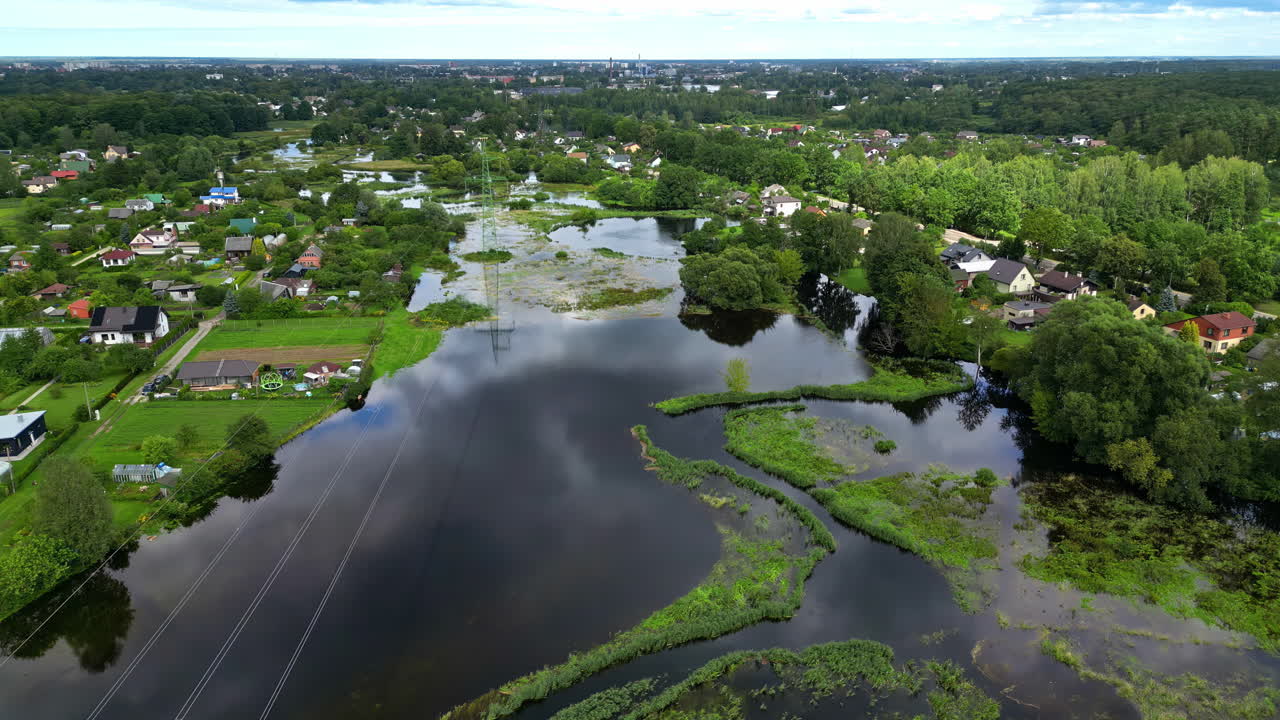 Drone shot of flooded and overflowing river at a small village with trees on a cloudy day with forest on the background and power lines in the foreground