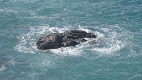 lone rock in ocean being pummeled by waves