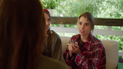 First-person-view-of-a-brunette-girl-chatting-with-two-girls,-they-are-sitting-in-a-gazebo-in-nature-and-drinking-tea.-Blonde-girl-in-a-red-plaid-shirt-and-a-girl-in-a-green-t-shirt