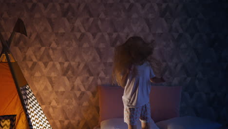 disobedient girl jumps on bed near play teepee in dark room