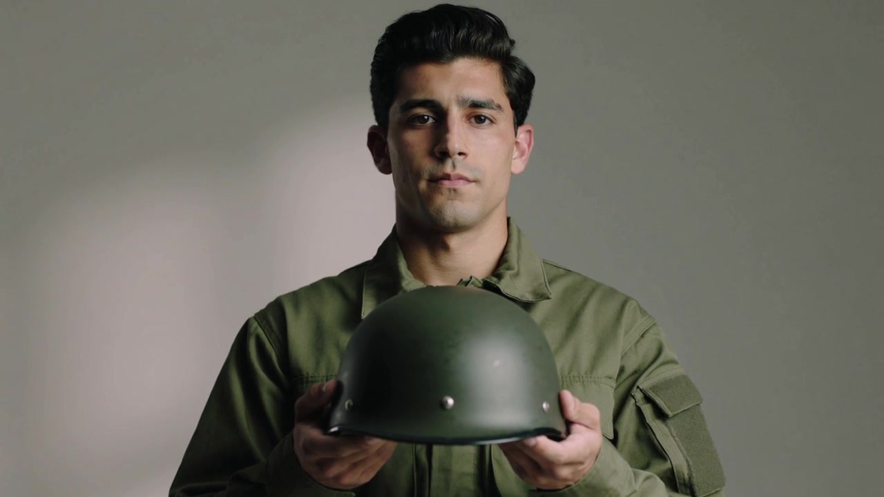 La telecamera inizia a riprendere un uomo in giacca color oliva che tiene un casco verde al petto in studio, per onorare la memoria.