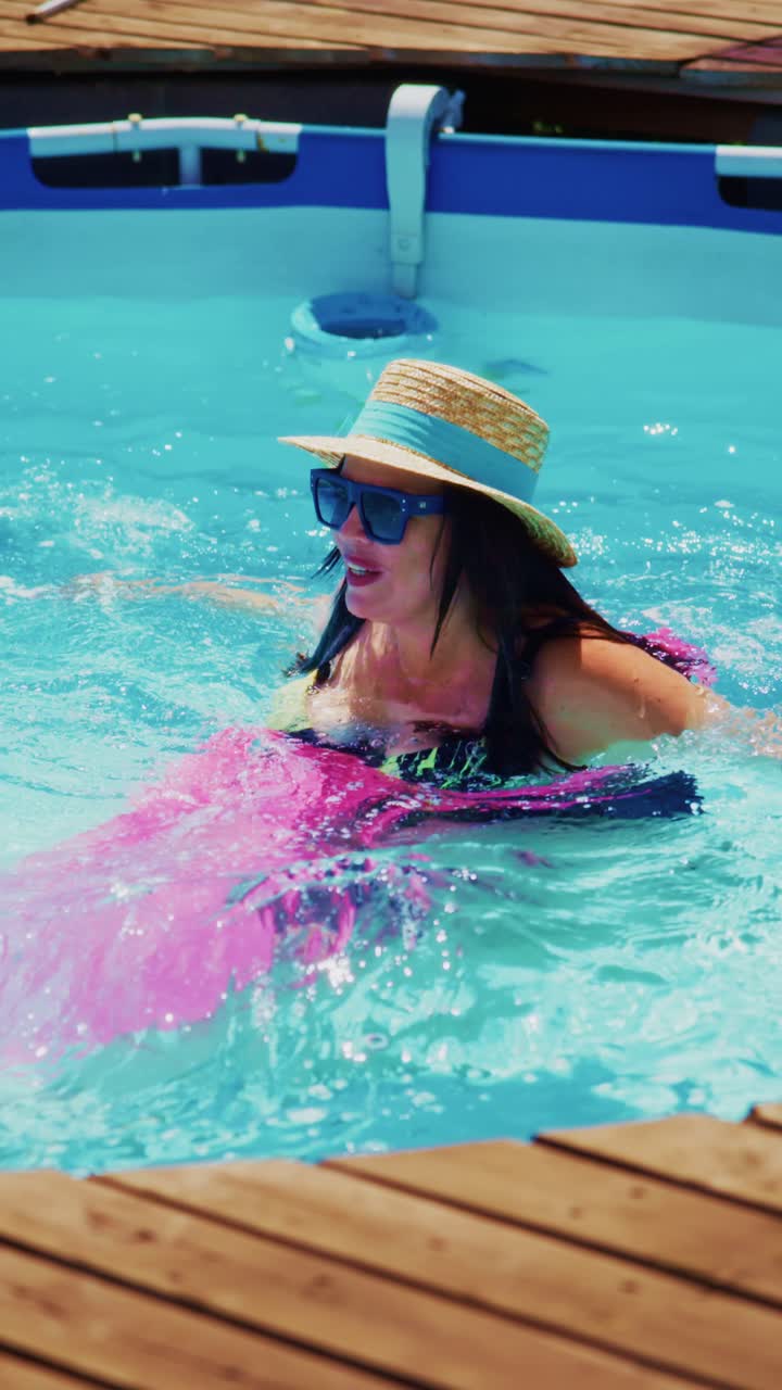 Joyful Moments of Summer: A Woman Enjoys Swimming in a Pool with a Colorful Float, Sporting Sunglasses and a Straw Hat Under Bright Sunlight