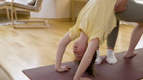 girl in sportswear doing urdhva dhanurasana pose while her mother helps her