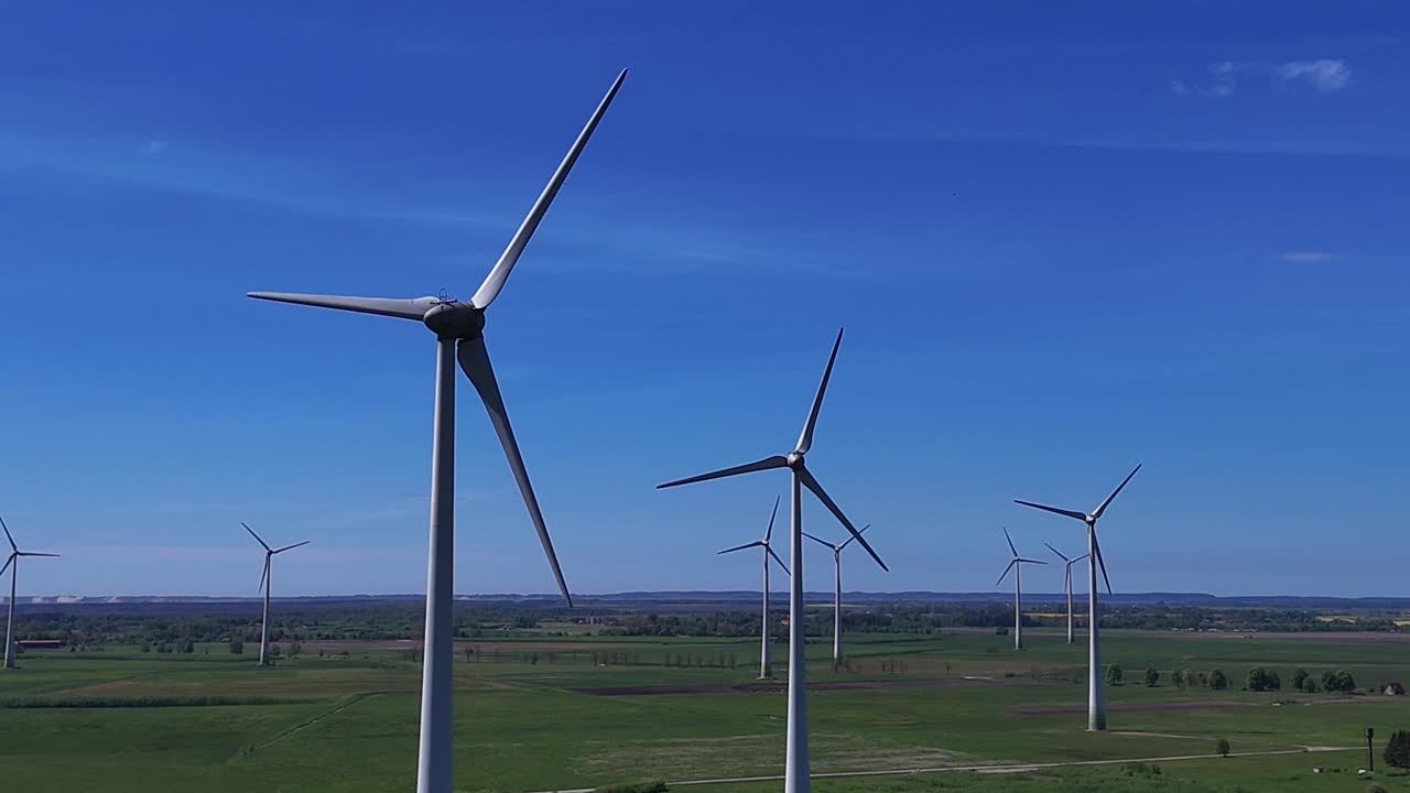 Wind turbines rotating on a vast green field under a clear blue sky