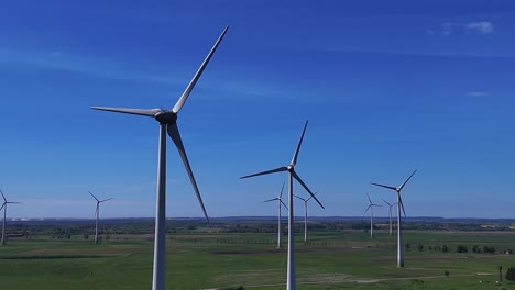 wind turbines rotating on a vast green field under a clear blue sky