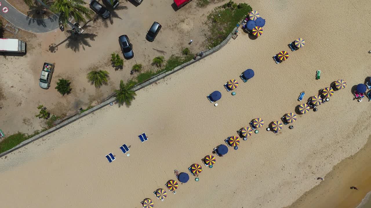 공중 촬영은 은 하늘 아래 활기찬 해안 분위기를 보여주는 우산과 의자를 가진 조용한 푸켓 해변을 포착합니다.