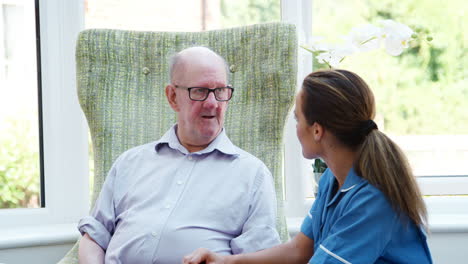 Senior-Hombre-Sentado-En-Una-Silla-Y-Hablando-Con-La-Enfermera-En-La-Casa-De-Retiro