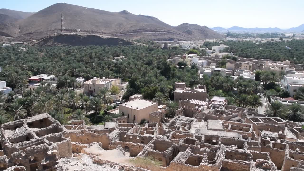 casas en ruinas en birkat al mouz en omán, con palmeras y montañas en el fondo