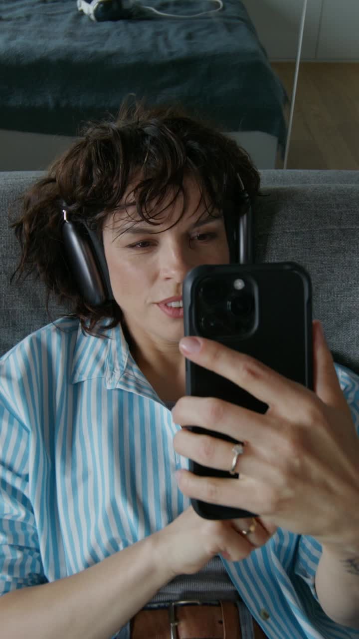 mujer relajándose en el sofá usando un teléfono inteligente con auriculares