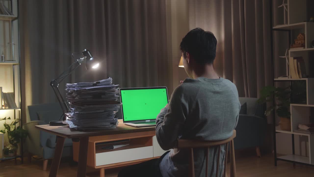 집 에서 문서 를 작업 하는 동안 녹색 스크린 노트북 과 대화 하는 아시아인 의 뒷면