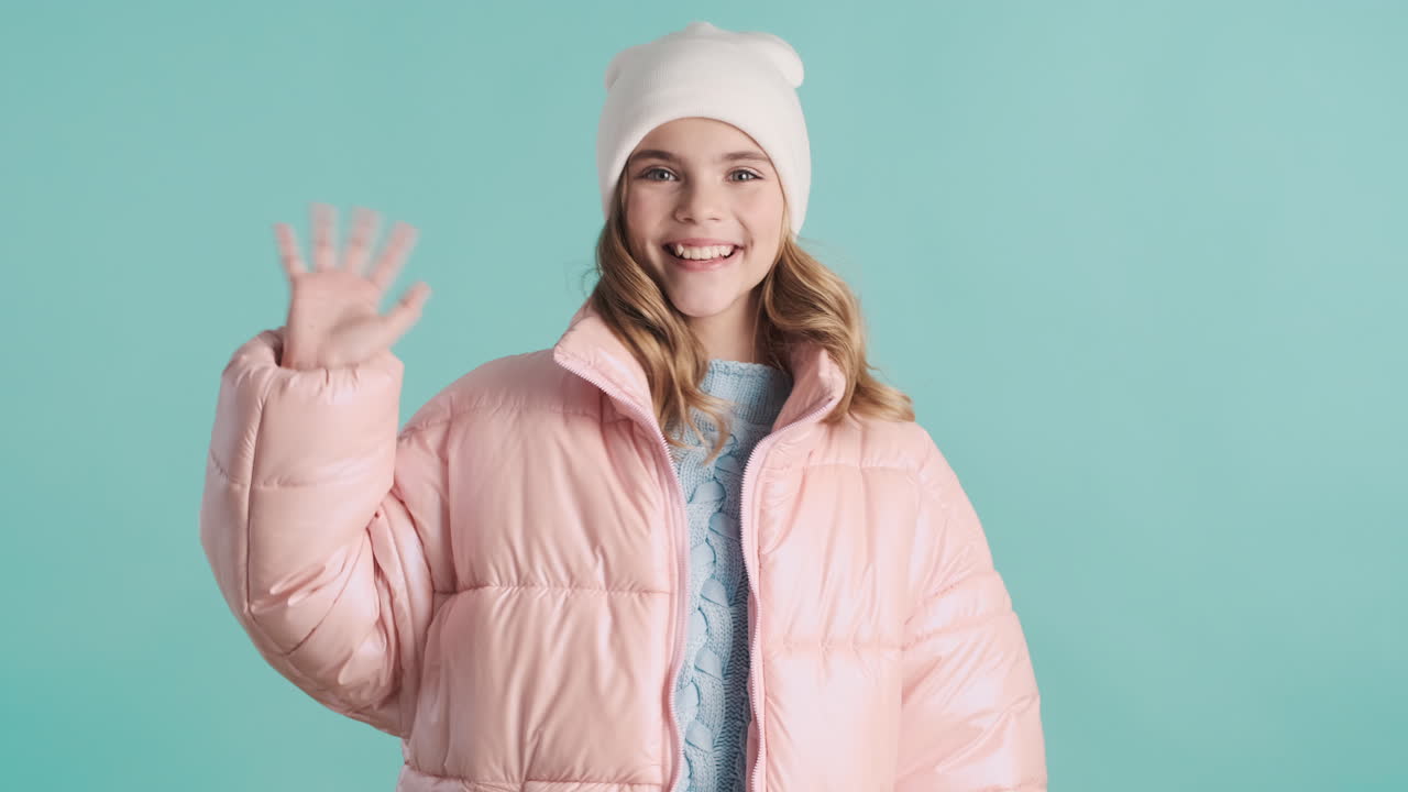 Teenage Caucasian girl with winter clothes waving to the camera.