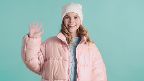 teenage caucasian girl with winter clothes waving to the camera.