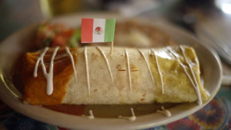 a delightful video captures an authentic burrito adorned with savory white sauce and accompanied by a mexican flag, enhancing the essence of this traditional mexican cuisine