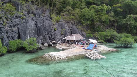 isolated hut dwelling on rock pile jutting into clear sea water on tropical island shore