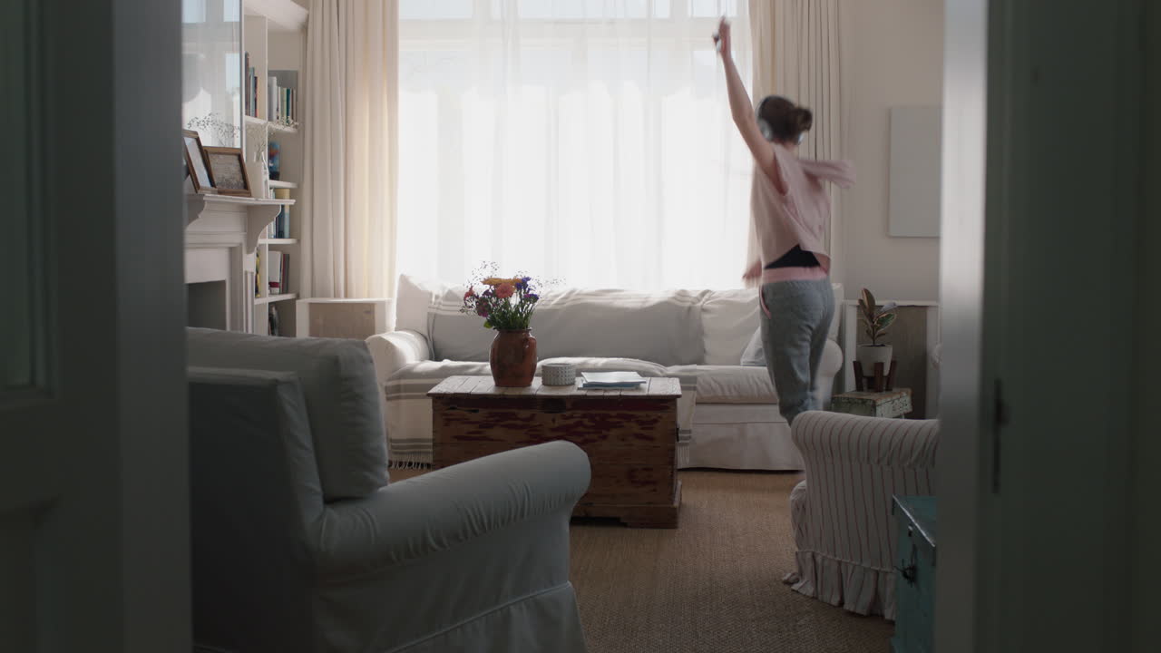 행복한 십대 소녀는 집에서 춤을 추고 즐겁게 음악을 듣고 헤드폰을 착용하고 재미있는 춤 움직임으로 주말 축제를 즐기고 있습니다.