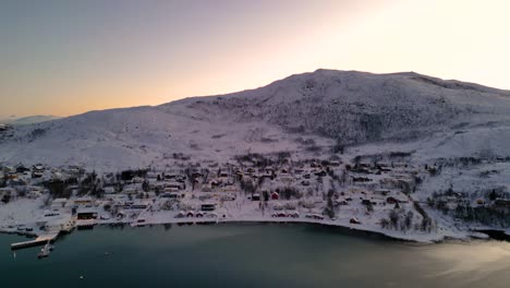 snow-covered village by the sea during sunrise, with warm light on the horizon at ersfjordvegen