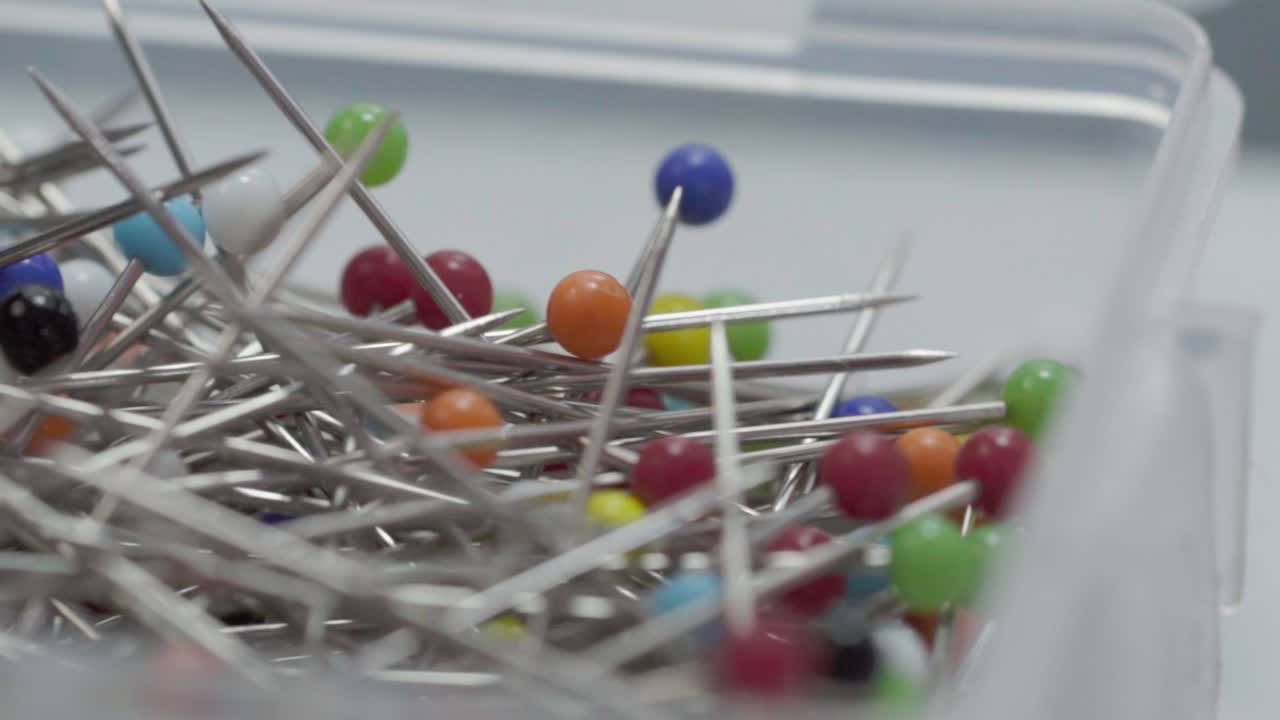 Close up of colorful metallic sewing pins with round heads stored inside transparent plastic box