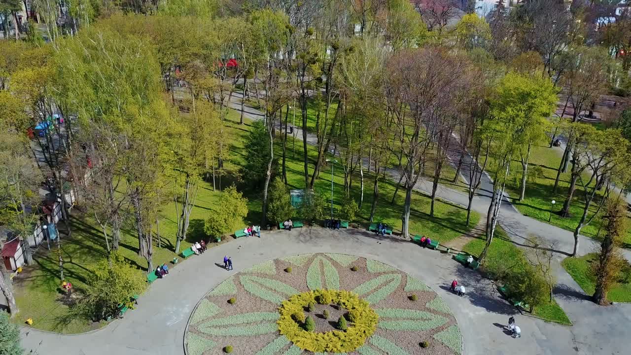 Beautiful park in the city center. Natural view of a park with people walking. Urban background with buildings. Camera moves rising up. Aerial view.