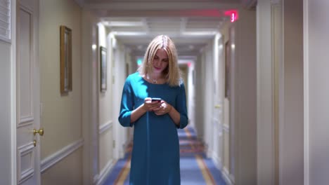 Young-woman-walking-on-long-corridor-on-hallway-and-looking-on-screen-smartphone