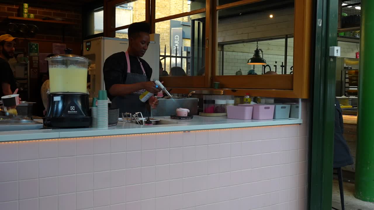Woman in apron making ice cream in a modern London dessert shop with a colleague nearby