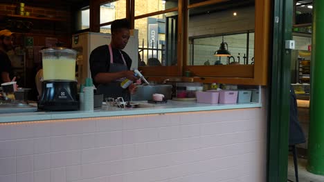 woman in apron making ice cream in a modern london dessert shop with a colleague nearby