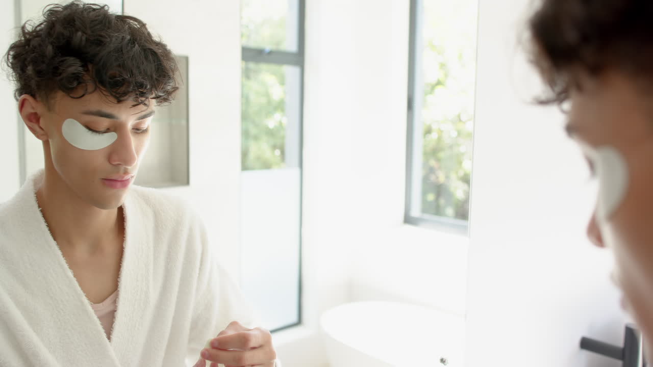 Applying under-eye patches, person in bathrobe looking in mirror at home