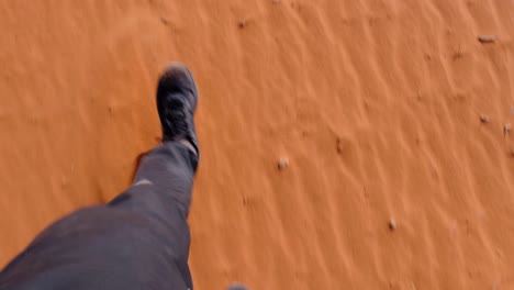 Top-down-view-of-legs-and-shoes-walking-across-the-vast,-remote-red-sandy-desert-of-Wadi-Rum-in-Jordan