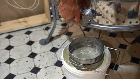 man opens the faucet at honey extracting machine. fresh golden organic liquid honey flows into the bucket standing under the equipment.