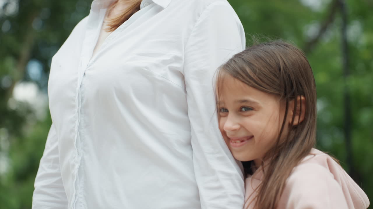 Mamma che ride con la figlia al parco in primo piano, ritratto spontaneo che cattura un sorriso genuino e un caloroso contatto visivo su uno sfondo di foglie, emozione naturale, connessione familiare giocosa e atmosfera luminosa