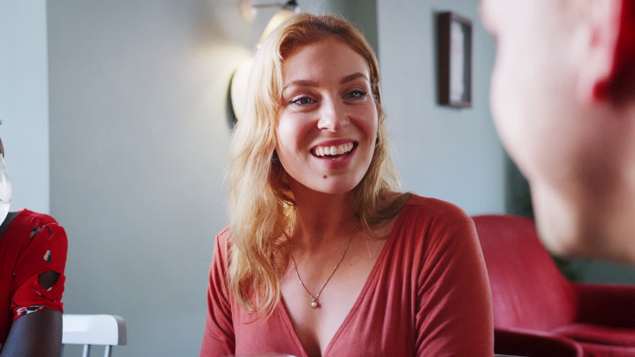Young blonde woman sitting with colleagues at table in a pub, listening with interest to her friend talking, over shoulder view, close up