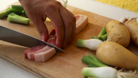 close up of male hand cutting pork belly on wooden cutting board into strips