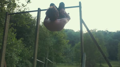 Fit youth doing sit ups outdoors on pull up bar upside down topless core strengthening exercise