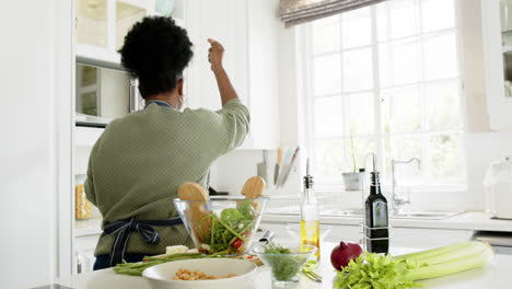 happy african american senior woman dancing with smartphone and headphones in kitchen, slow motion