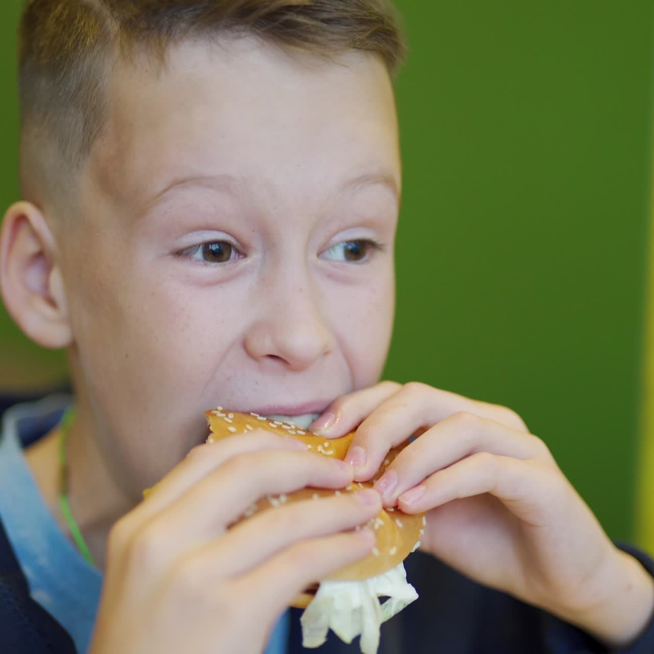 Hungry child biting burger in a restaurant. Fast food cafe. Harmful nutrition