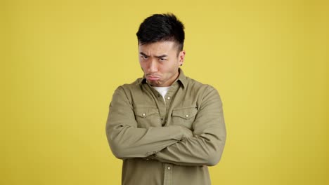 man with unhappy and pouting expression with crossed arms on yellow background