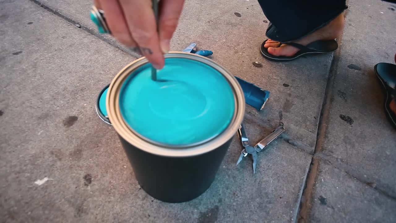 Man with turquoise ring mixing blue paint on the sidewalk to prepare for painting art