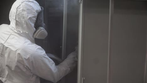 trabajador industrial que aplica recubrimiento en polvo a armarios metálicos