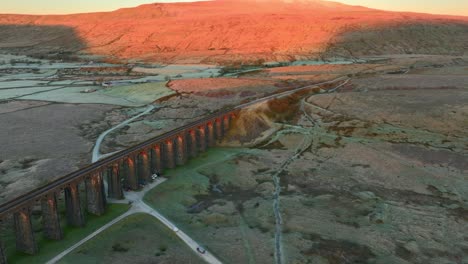 luz del amanecer de invierno iluminando grandes arcos de colinas y puentes ferroviarios con furgonetas de trabajo que se acercan a la carretera