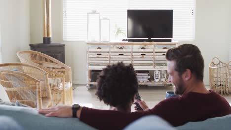 video of back view of happy diverse couple drinking coffee and watching tv with copy space
