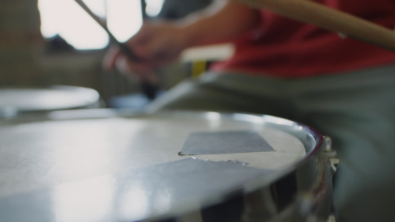 Close-up of a drum and drumstick with a person playing drums in the background