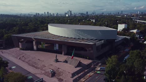 Orbital-shot-of-the-National-Auditorium-of-Mexico-on-a-sunny-morning,-the-national-flag-flies-on-its-flagpole-on-the-facade-of-the-building