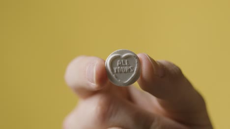 primer plano de la mano que sostiene caramelos de corazón con todo tu mensaje sobre fondo amarillo