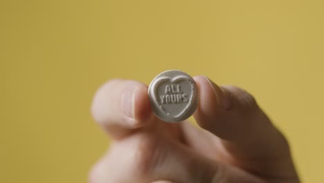 close up of hand holding heart candy with all yours message on yellow background